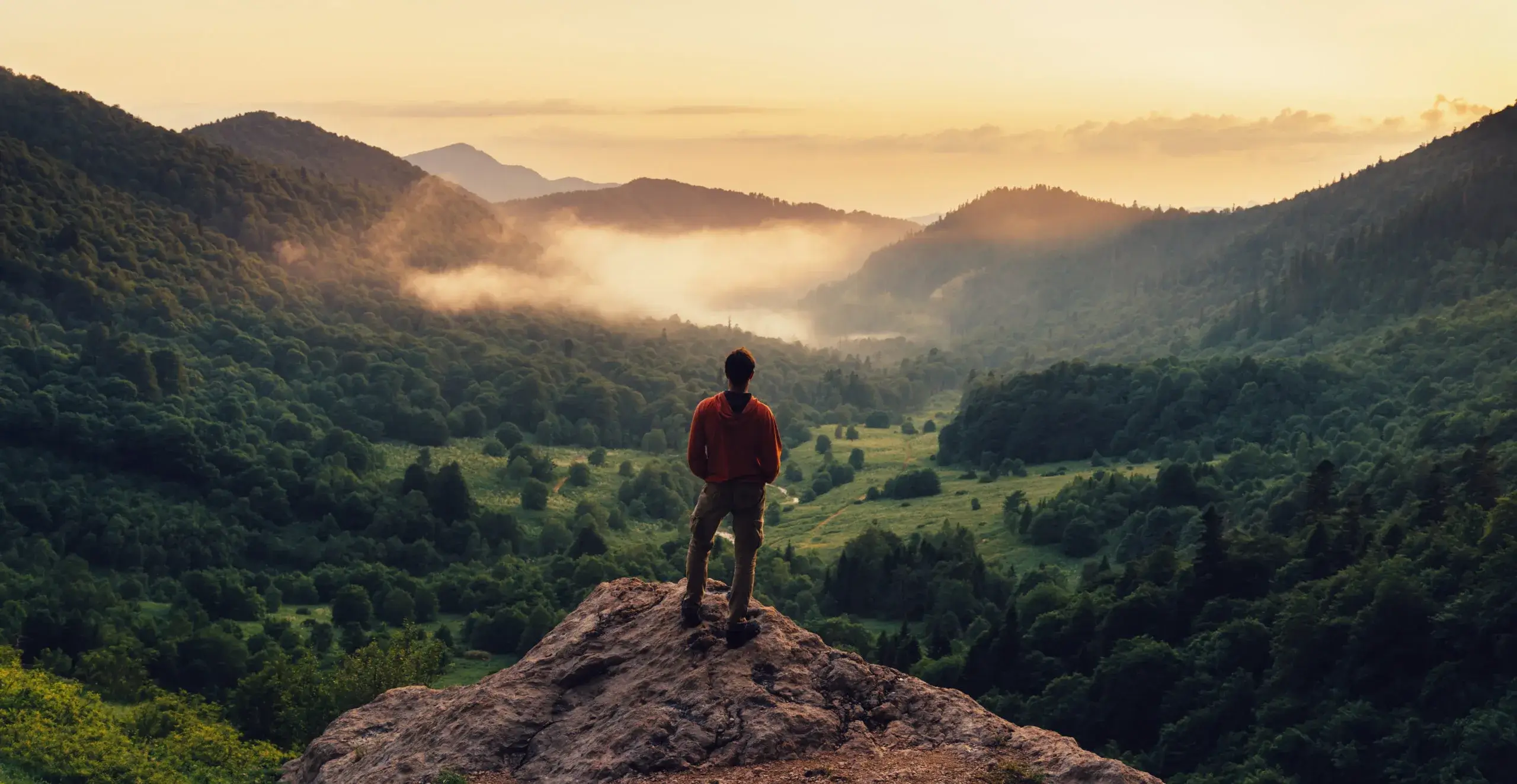 A lone hiker on a ridge overlooking a vast mountain range.