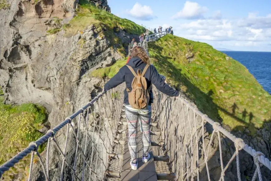 A mountain guide helping a traveler cross a rope bridge.