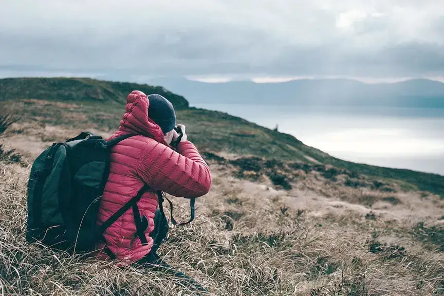 A backpack with a camera and a map lying on a rock.